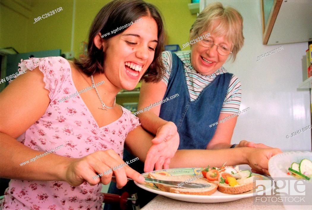Stock Photo: Carer assisting teenage girl with physical disability to prepare a sandwich in kitchen of residential respite care home,.