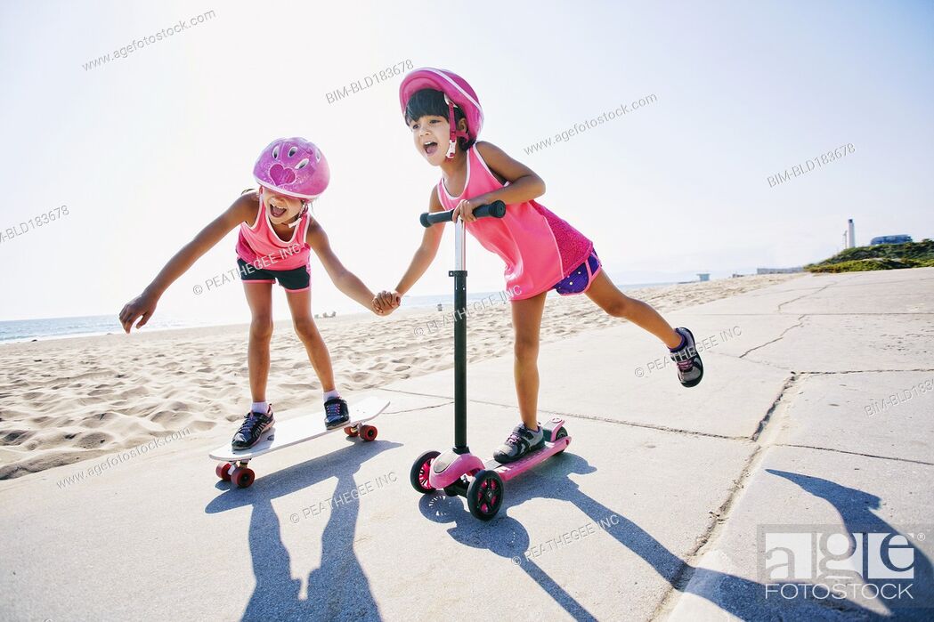 Stock Photo: Girls riding skateboard and scooter at beach.