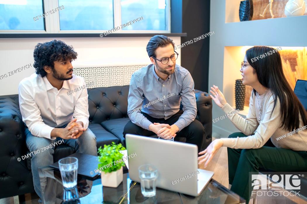 Stock Photo: Young company worker sitting with her male colleagues around the coffee table during the meeting.