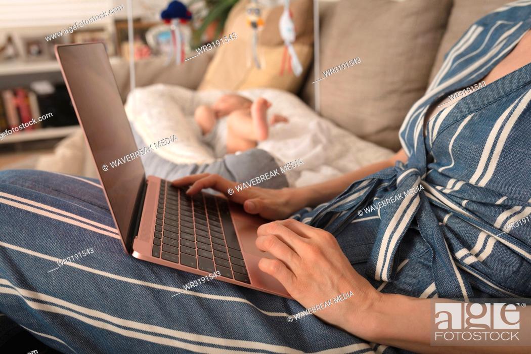 Stock Photo: Mother working on laptop baby lying in crib besides her at home.