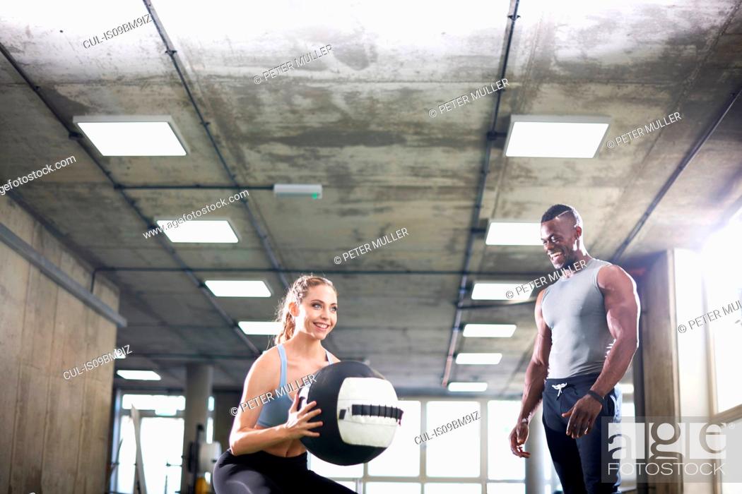 Stock Photo: Trainer watching female client lift medicine ball in gym.