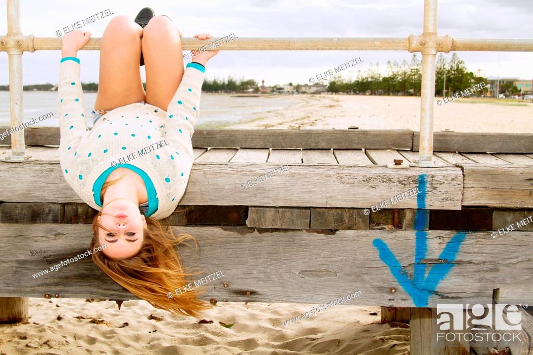 Stock Photo: Young woman hanging upside down from pier.