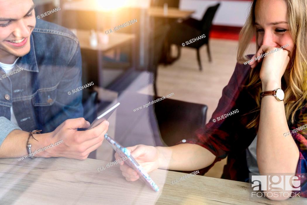 Stock Photo: Male and female students looking at smartphone in cafe window seat, view through window.