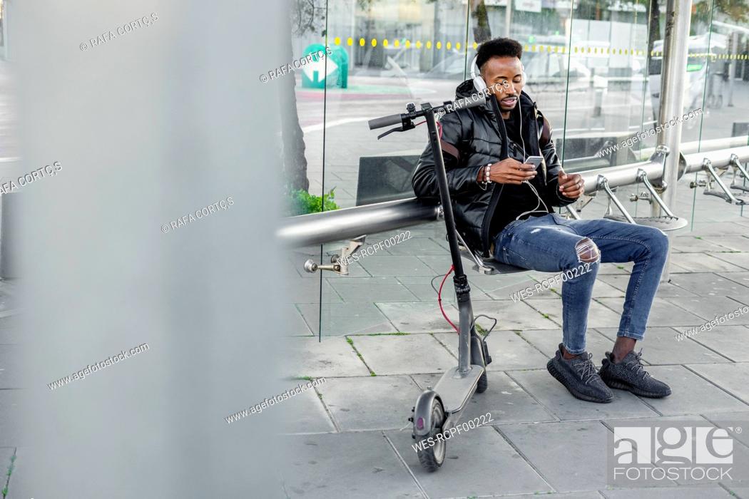 Stock Photo: Man with smartphone and e-scooter at bus stop.