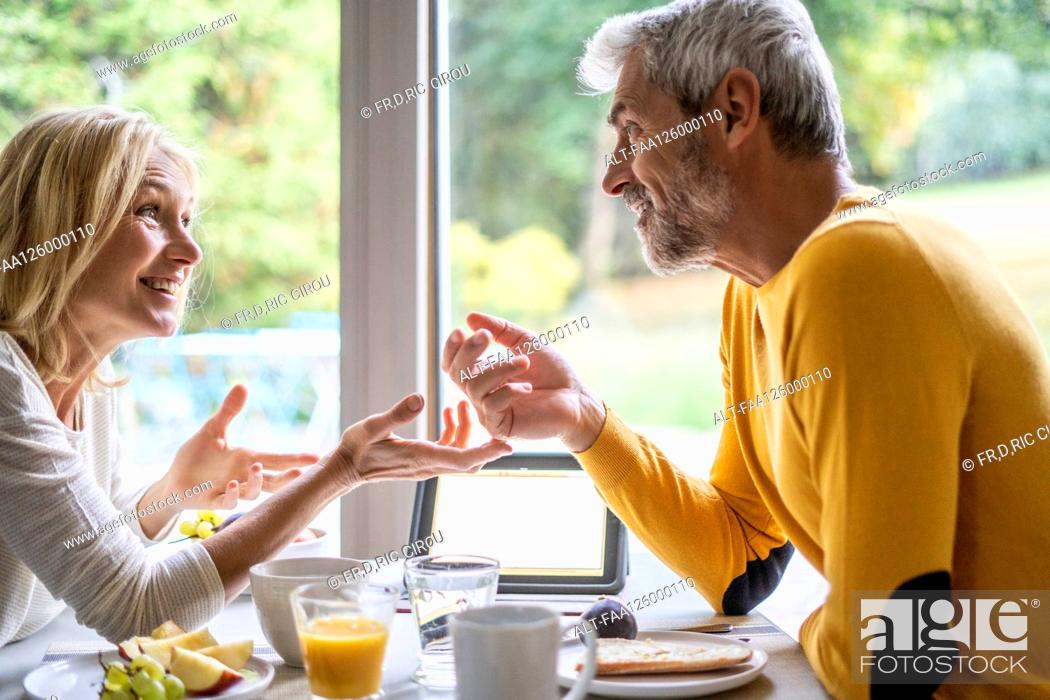 Imagen: Smiling mature couple talking with each other while having breakfast.