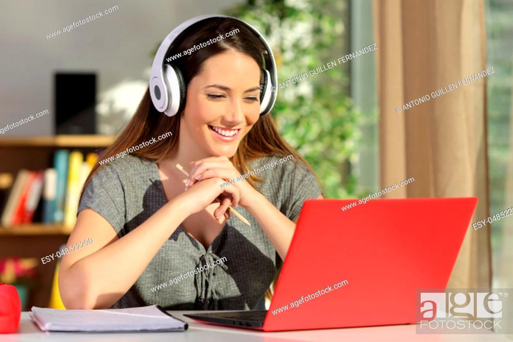 Stock Photo: Portrait of a beautiful student viewing and listening video tutorials on line with headphones and a red pc sitting in a table at home.