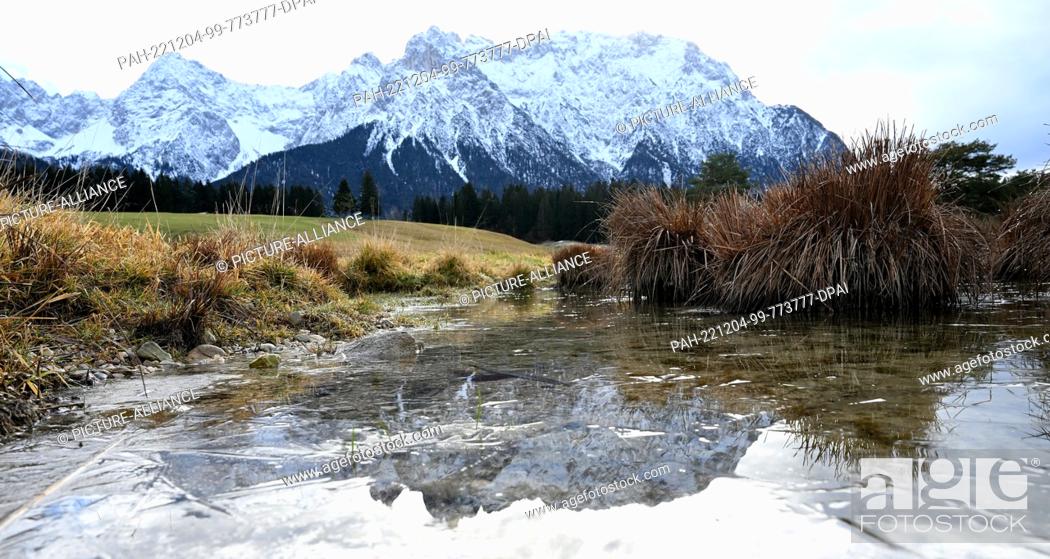 Stock Photo: 04 December 2022, Bavaria, Klais: The Karwendel Mountains are reflected on a thin layer of ice on Lake Schamlen. Photo: Angelika Warmuth/dpa.