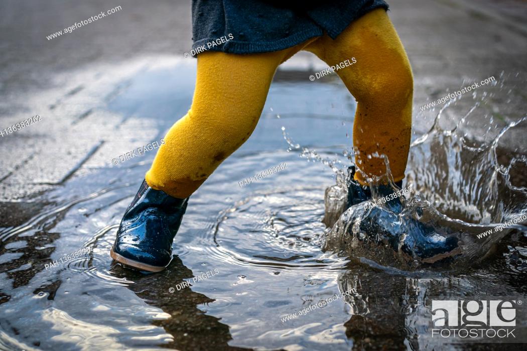 Stock Photo: October 7th, 2020, Trebbin, a little girl with rubber shoes and yellow tights jumps around in a puddle and has a lot of fun. | usage worldwide.