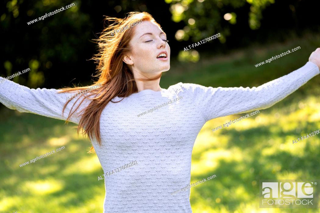 Photo de stock: Young woman with eyes closed stretching her arms in park.