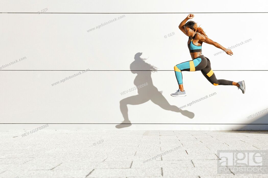 Stock Photo: Young woman running against white wall at city.