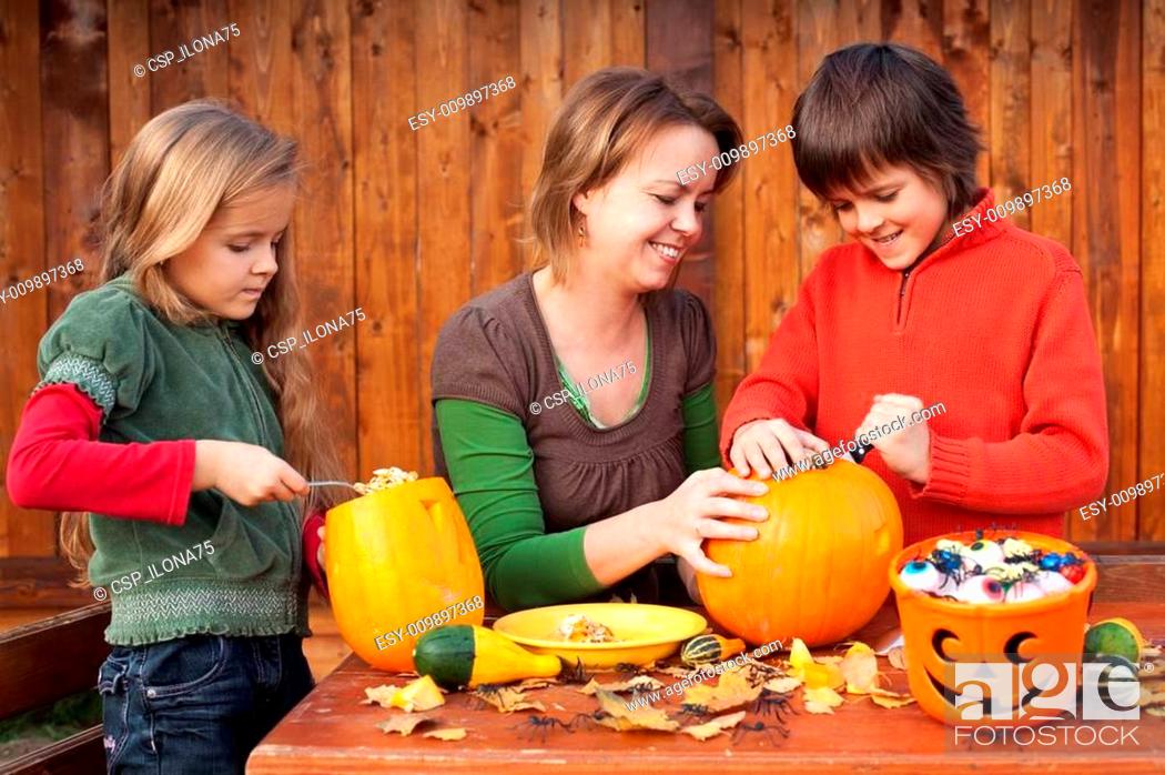 Stock Photo: Woman helping kids to carve their Halloween jack-o-lantern.