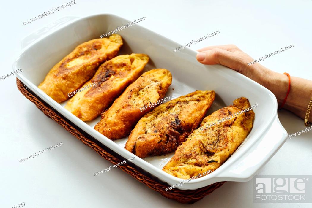 Stock Photo: Female hand holding a tray with torrijas, a typical Spanish sweet fried toasts of sliced bread soaked in eggs and milk, on white background.