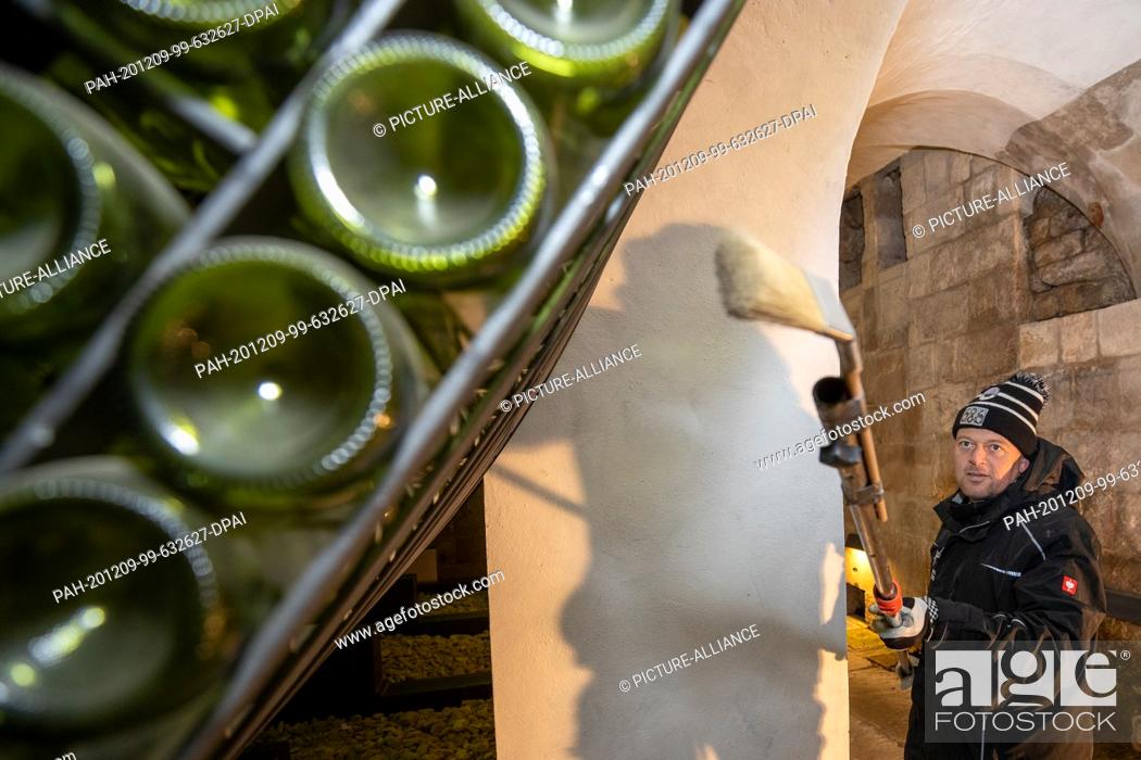 Stock Photo: 04 December 2020, Saxony, Königstein: Jens Hickmann cleans with a brush and an extension from the outside over the wine bottles.