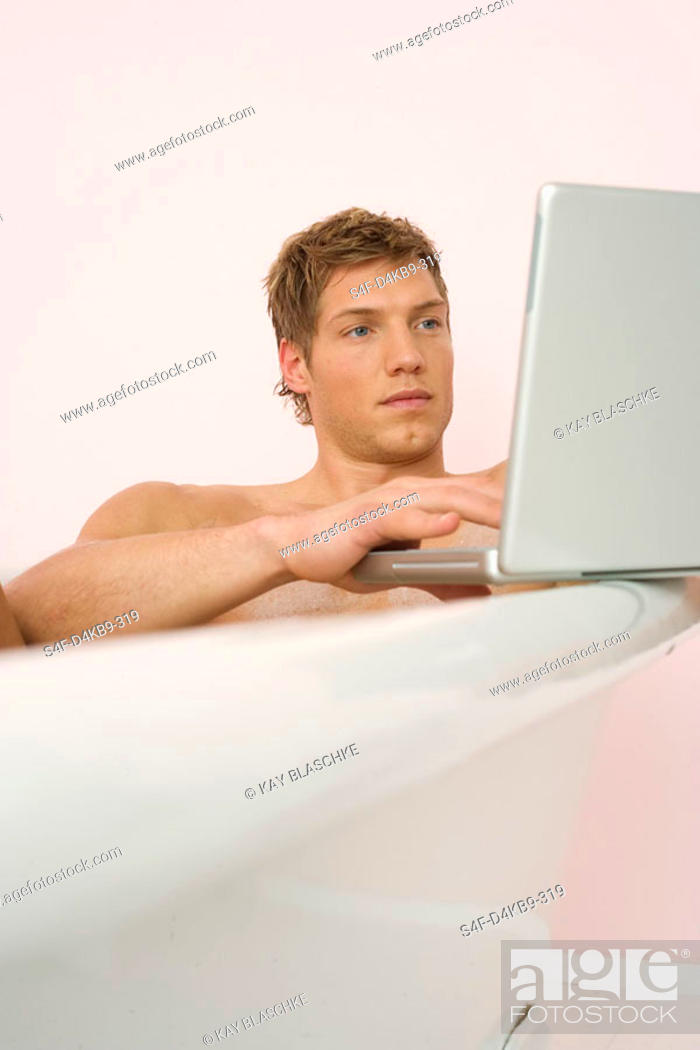 Stock Photo: Man sitting in a bathtub, using a laptop.