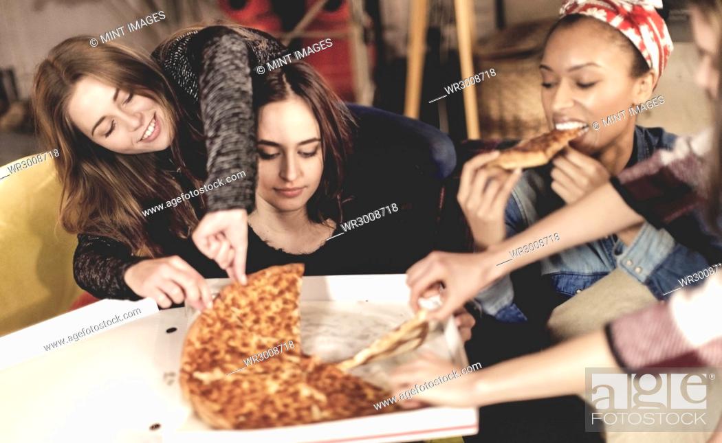 Stock Photo: Four young women sitting round a table, eating pizza.