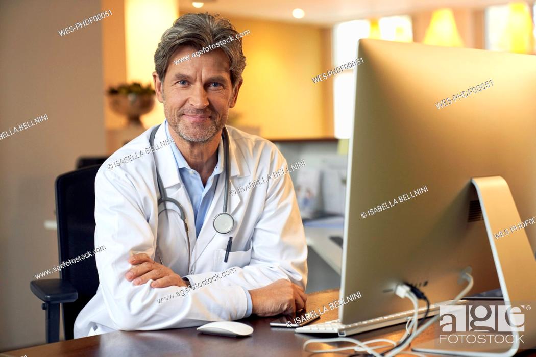 Stock Photo: Portrait of confident doctor at desk in his medical practice.