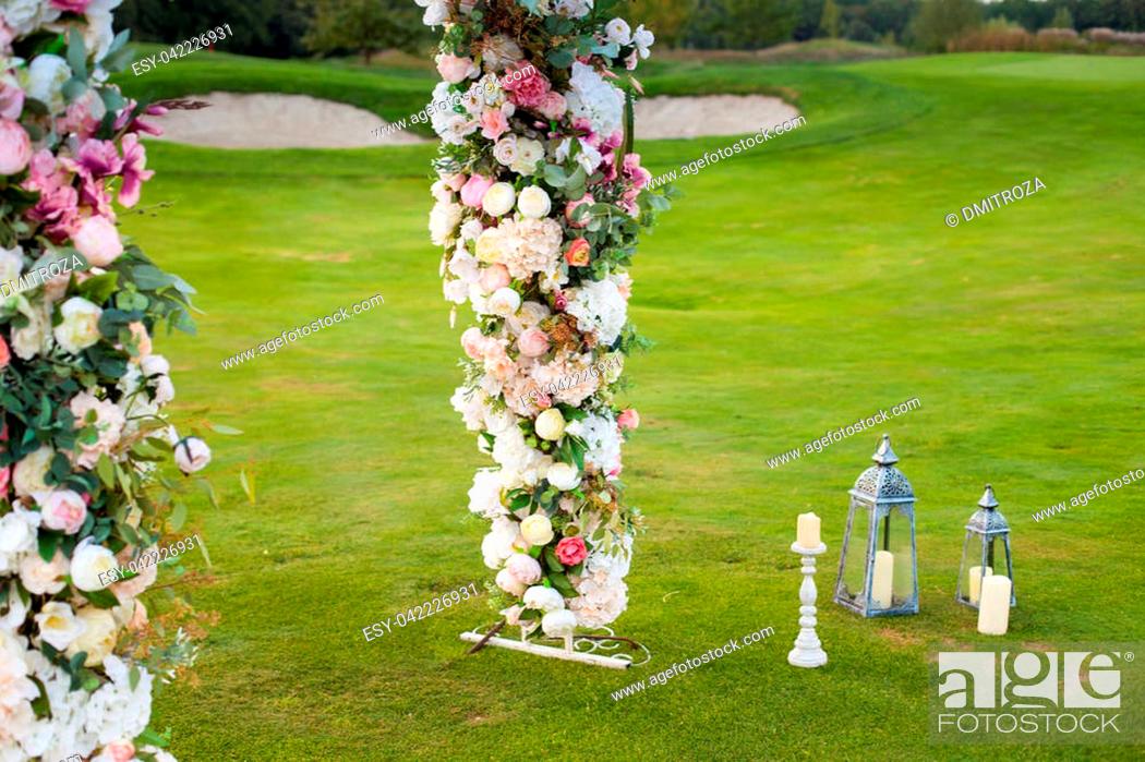 Stock Photo: Beautiful floral arch with lots of small pink, purple and white flowers on the green field on the backgroung of the forest with white candles standing nearby.