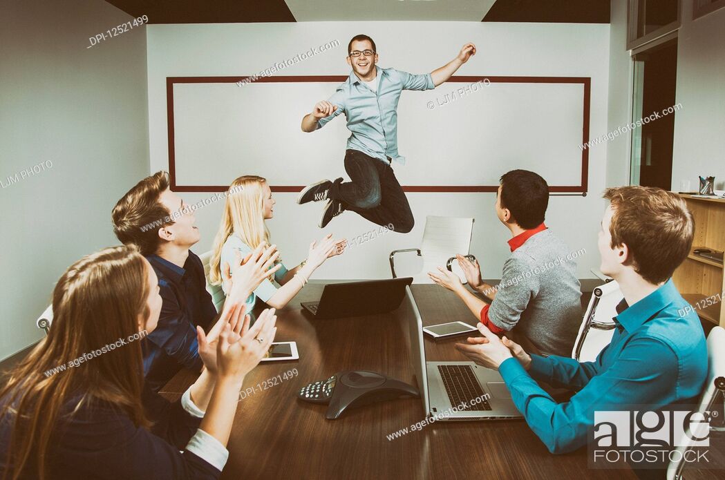 Stock Photo: Young millennial business professional jumping to celebrate an accomplishment with his co-workers working in a conference room during a presentation and one of.