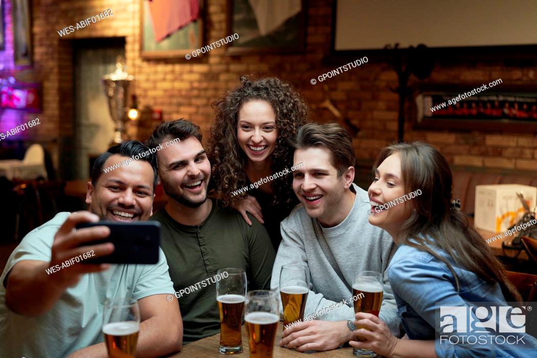 Stock Photo: Group of happy friends having beer and taking a selfie in a pub.
