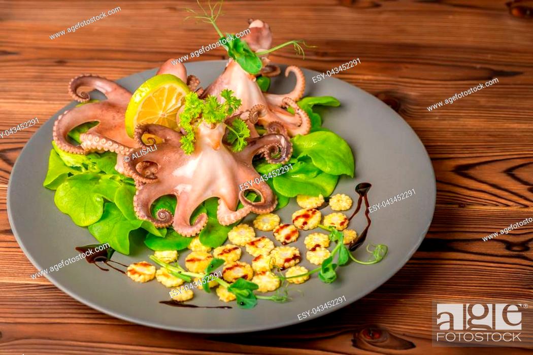 Stock Photo: boiled whole octopus served with lime, corn, cucumber and sprig of pea leaves on plate, seafood.