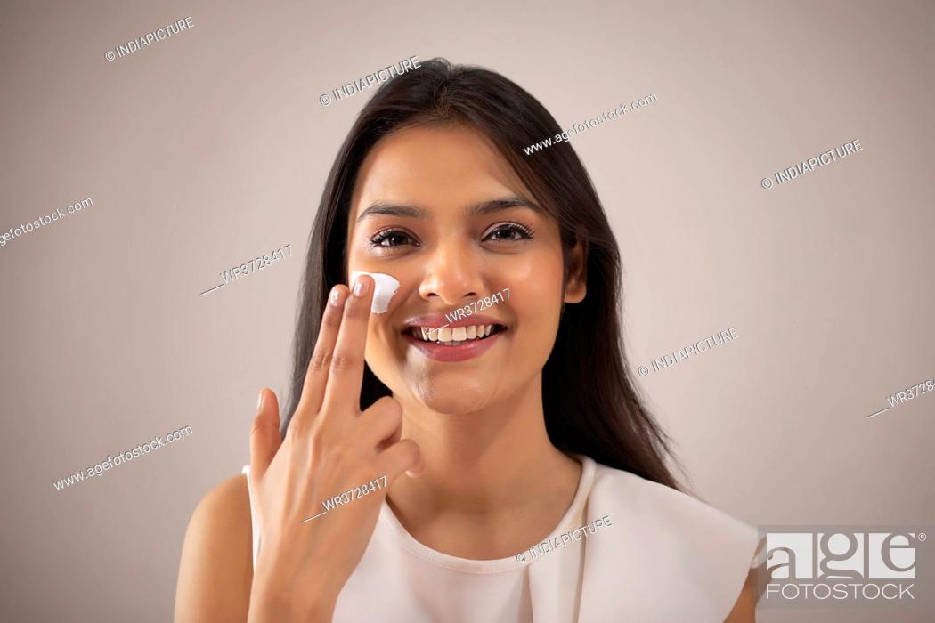 Stock Photo: A YOUNG WOMAN HAPPILY PUTTING CREAM ON FACE.