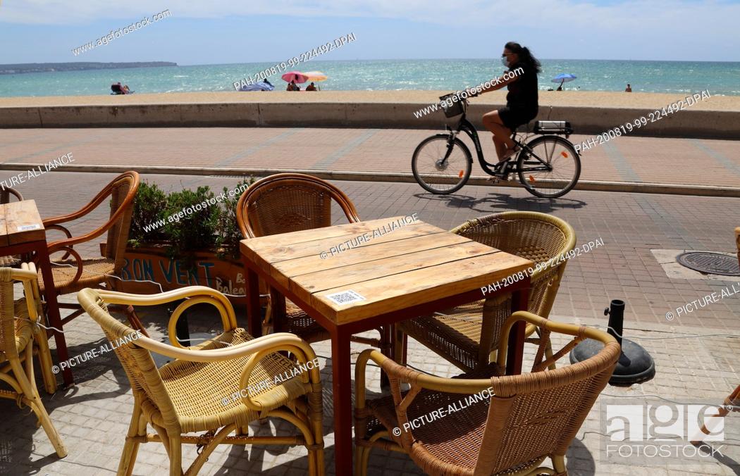 Photo de stock: 18 August 2020, Spain, Palma: A woman rides her bike in front of the empty terrace of a restaurant on the beach of Can Pastilla in Palma de Mallorca.