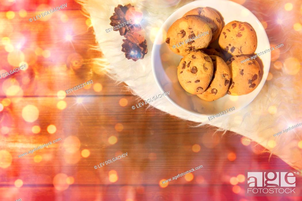 Stock Photo: holidays, christmas, winter, advertisement and food concept - close up of cookies in bowl and cones on white fur rug over lights.
