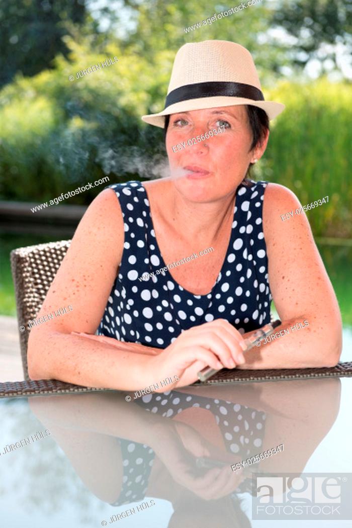 Stock Photo: attractive woman siiting by the pool and smoking e-cigarette.