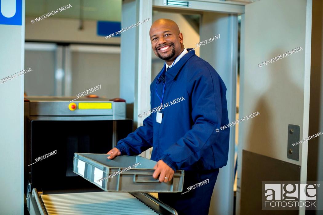 Stock Photo: Smiling airport security officer holding a crate near conveyor belt.