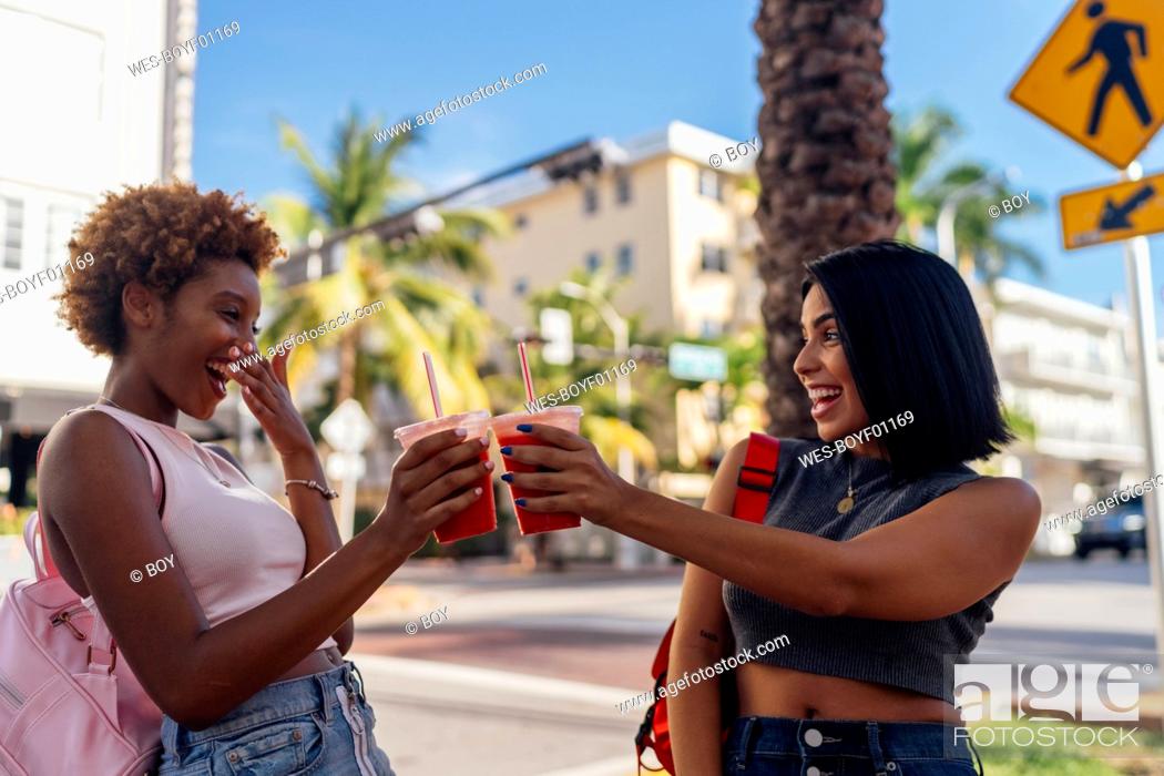 Stock Photo: USA, Florida, Miami Beach, two happy female friends having a soft drink in the city.