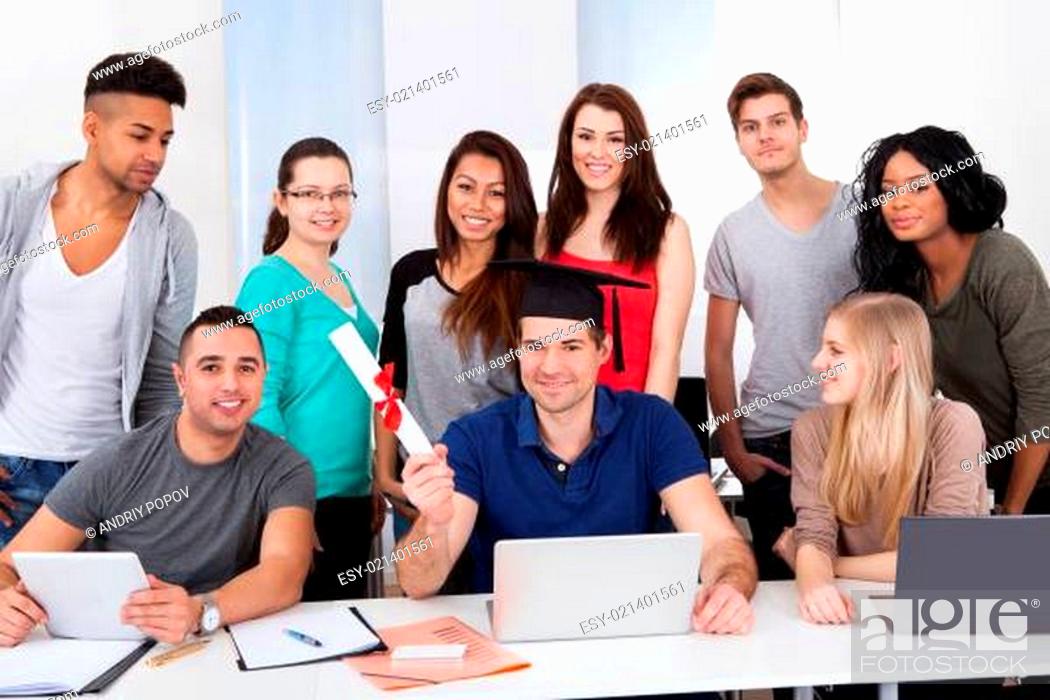 Stock Photo: College Student Holding Degree With Classmates Looking At Him.