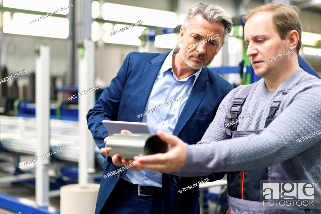 Stock Photo: Businessman and worker examining steel pipe in a factory.