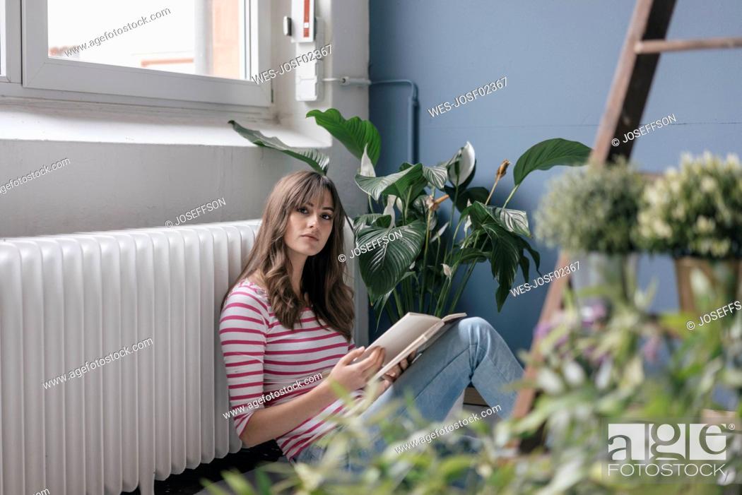 Stock Photo: Woman sitting on ground in her new home, reading a book, surrounded by plants.