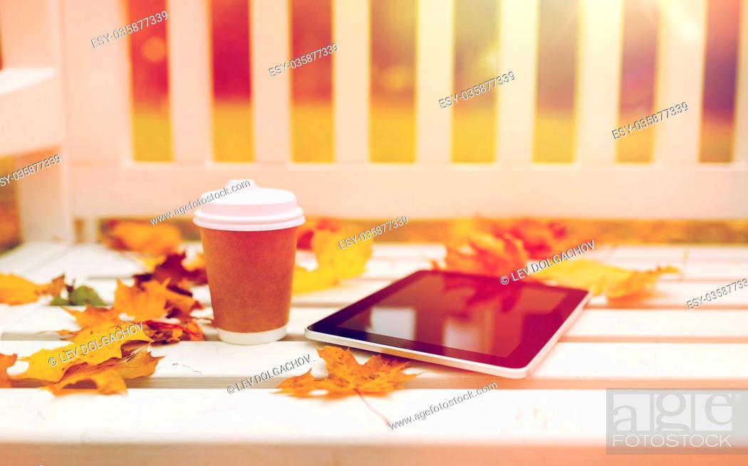 Stock Photo: season, technology and advertisement concept - tablet pc computer and coffee paper cup on bench in autumn park.