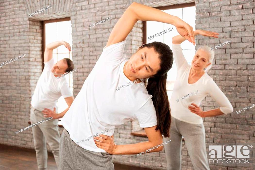 Stock Photo: Look at me. Positive delighted female standing behind her instructor keeping right hand above her head while putting left hand on the waist.