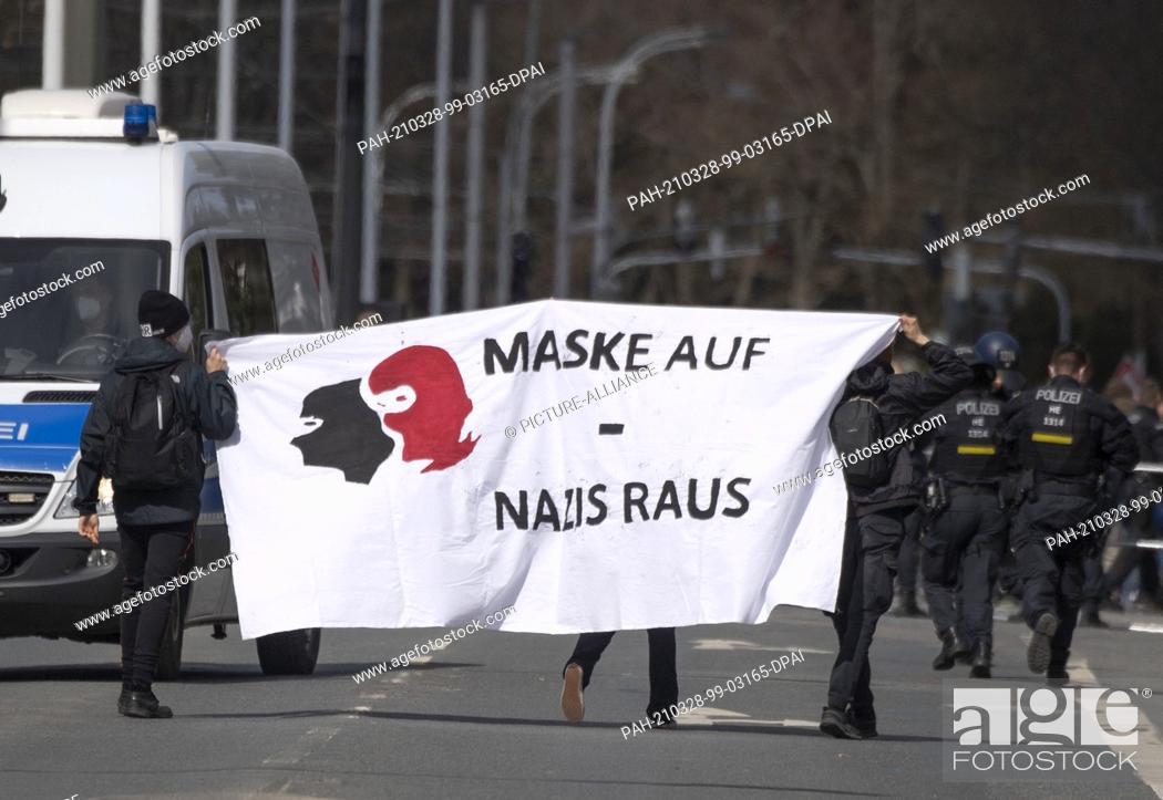 Stock Photo: 28 March 2021, Hessen, Darmstadt: With a poster with the inscription ""Mask on - Nazis out"" several people participate in a rally against a rally of the.