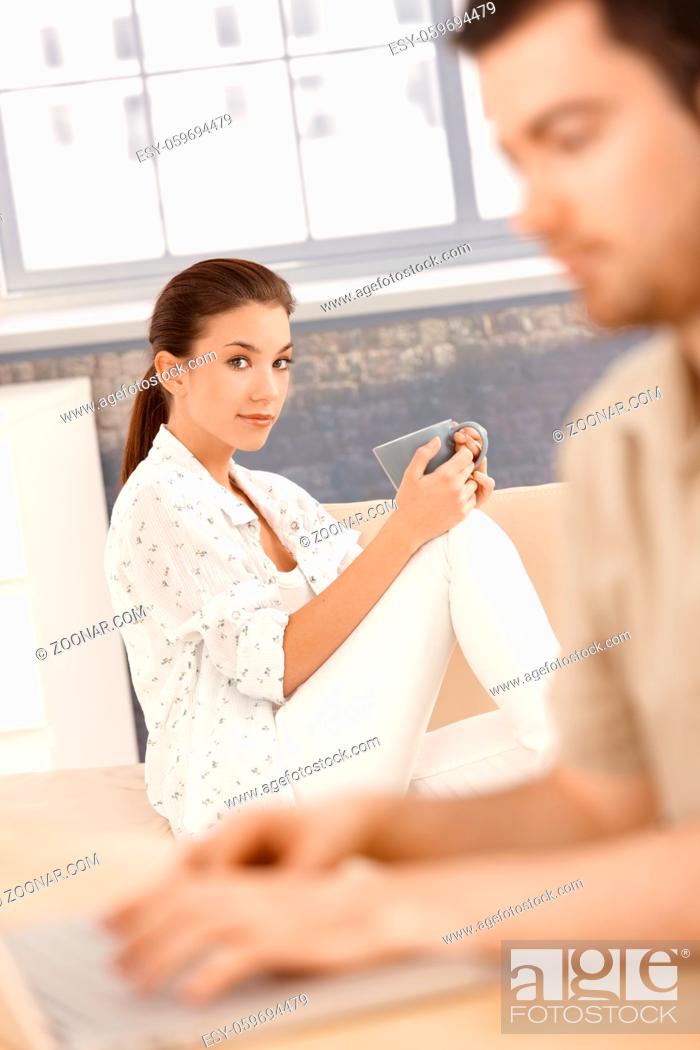 Photo de stock: Young woman sitting bored on sofa, man working on laptop.