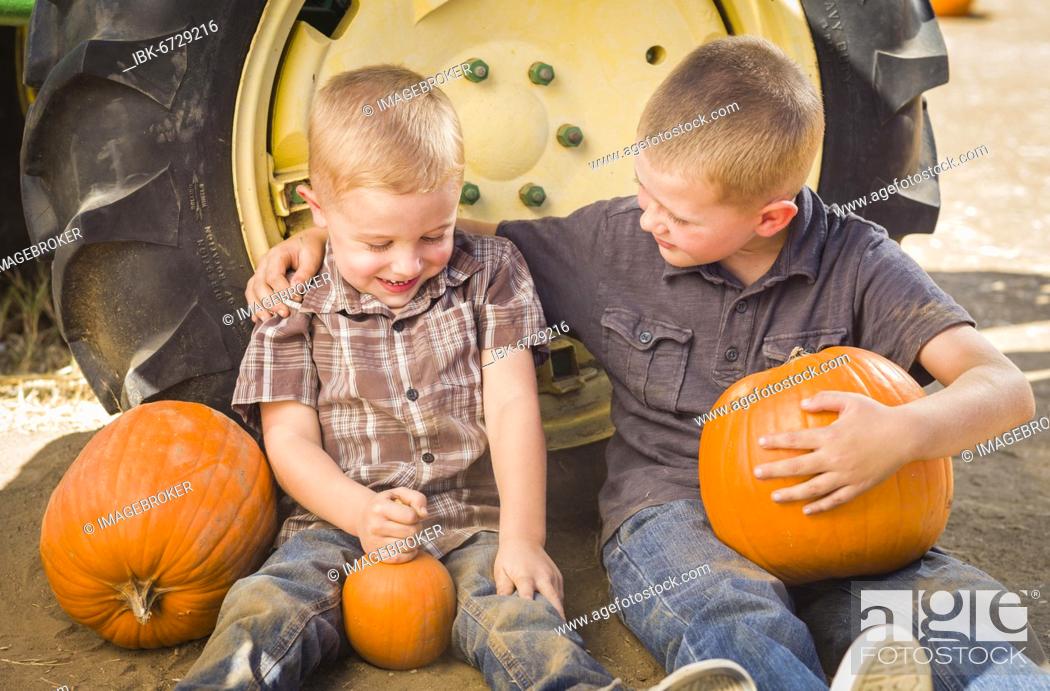 Stock Photo: Two boys sitting against a tractor-tire holding pumpkins and talking in rustic setting.