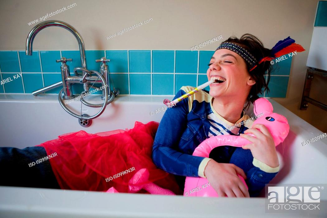 Stock Photo: Young woman in bath, wearing costume and blowing party blower.
