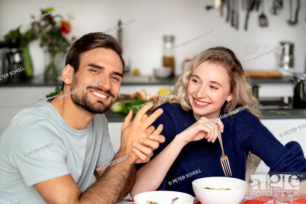 Photo de stock: Smiling blond woman looking at boyfriend sitting at table.