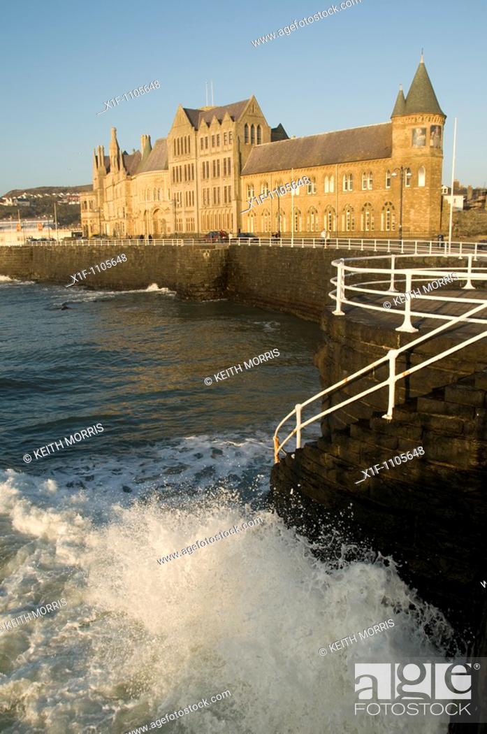 Stock Photo: wave crashing on sea wall by the old college building, aberystwyth university, wales UK.