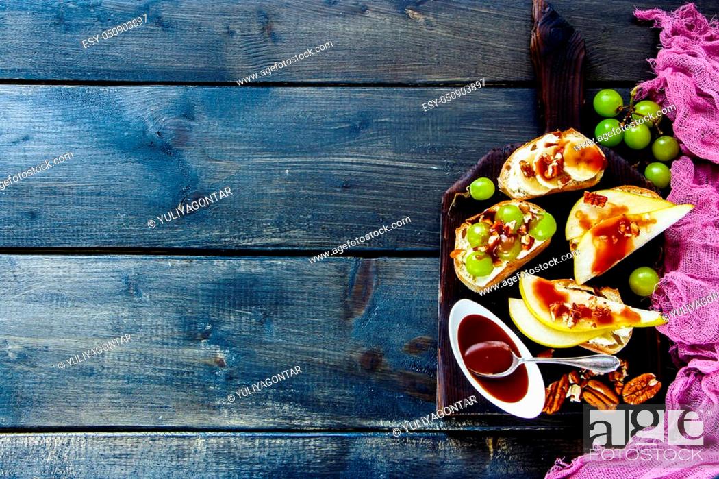 Stock Photo: Breakfast toasts or snack sandwiches on vintage chopping board over wooden background. Crostini with pear, cream-cheese, grapes, banana.