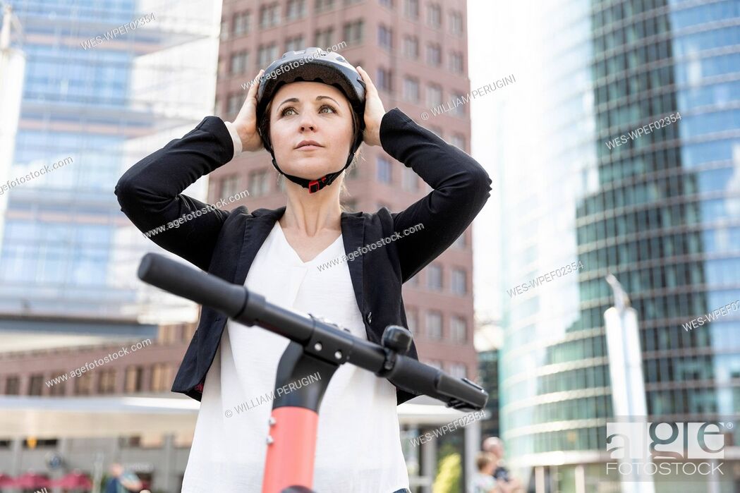Stock Photo: Woman with e-scooter in the city putting on helmet, Berlin, Germany.