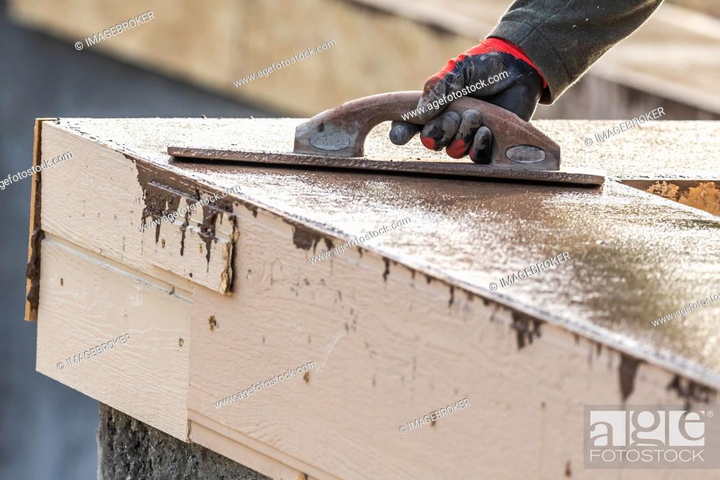 Stock Photo: Construction worker using wood trowel on wet cement forming coping around new pool.