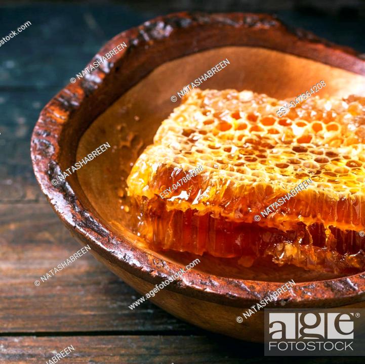 Stock Photo: Honeycomb in wooden bowl over old wooden table. Square image with selective focus.