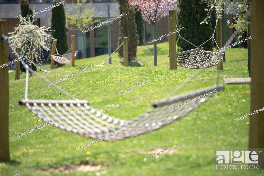 Stock Photo: PRODUCTION - 28 April 2021, Hessen, Fulda: Empty hammock hanging on the campus of Fulda University of Applied Sciences. Sitting alone in the children's room in.