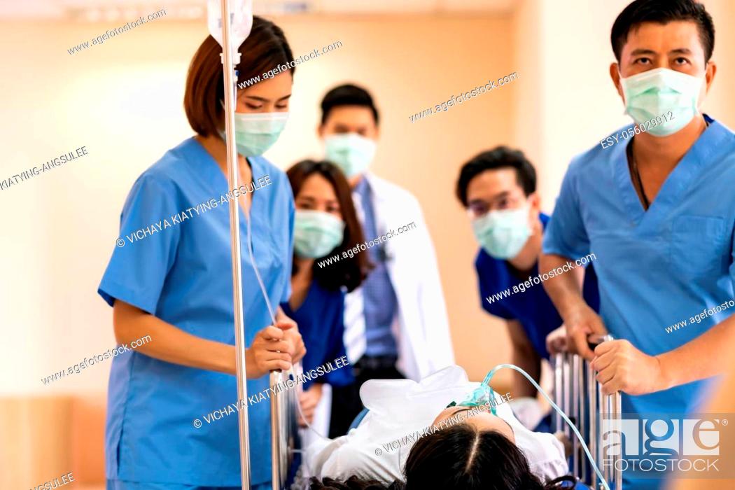 Stock Photo: Seriously injured patient with oxygen mask on gurney stretcher bed pushed by medical team of doctor nurse and paramedic to the Operating Room.