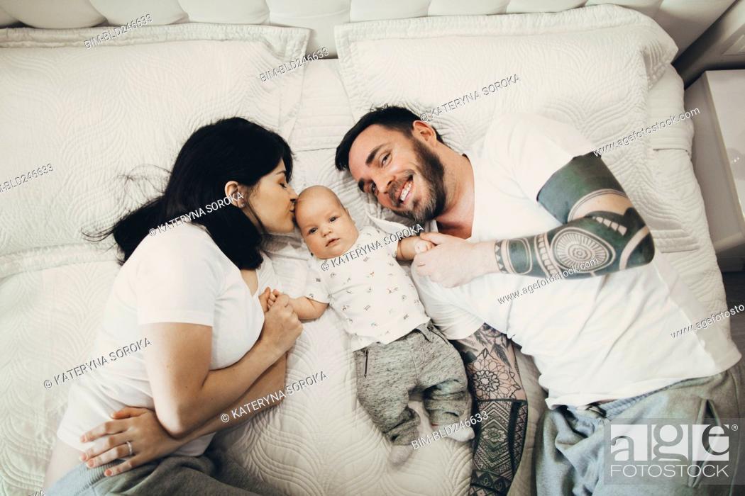 Stock Photo: Caucasian mother and father holding hands with baby son on bed.