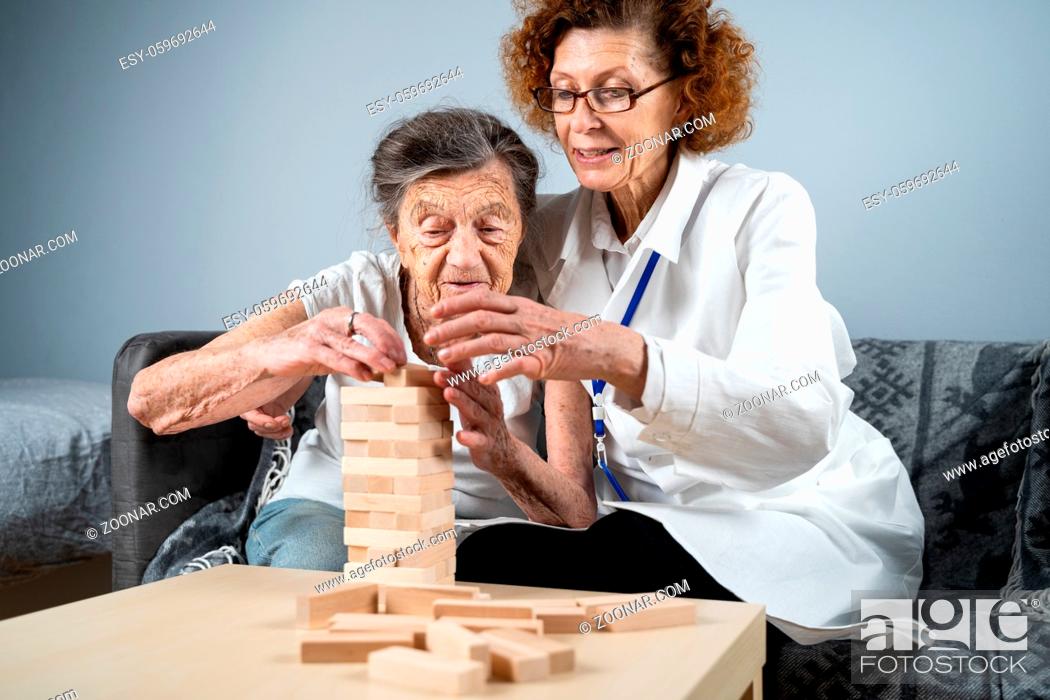 Stock Photo: Jenga game. Theme is dementia, aging and games for old people. Caucasian senior woman builds tower of wooden blocks with the help of a doctor as part of a.