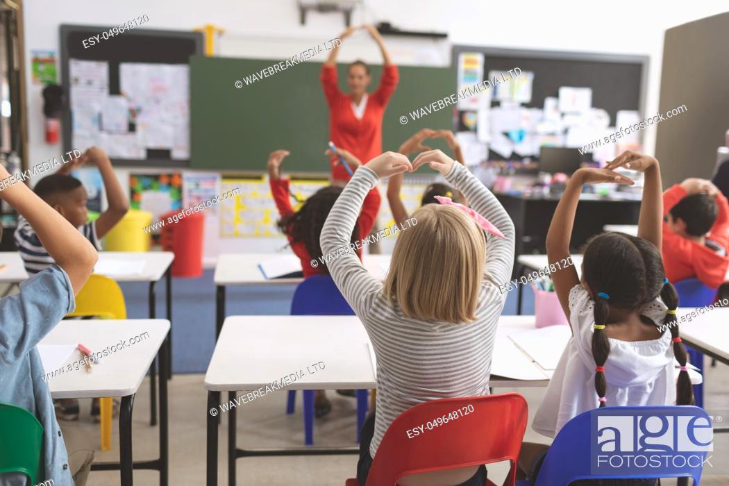 Stock Photo: Rear view of mixte ethnicity school kids with arms up playing in the classroom at school.